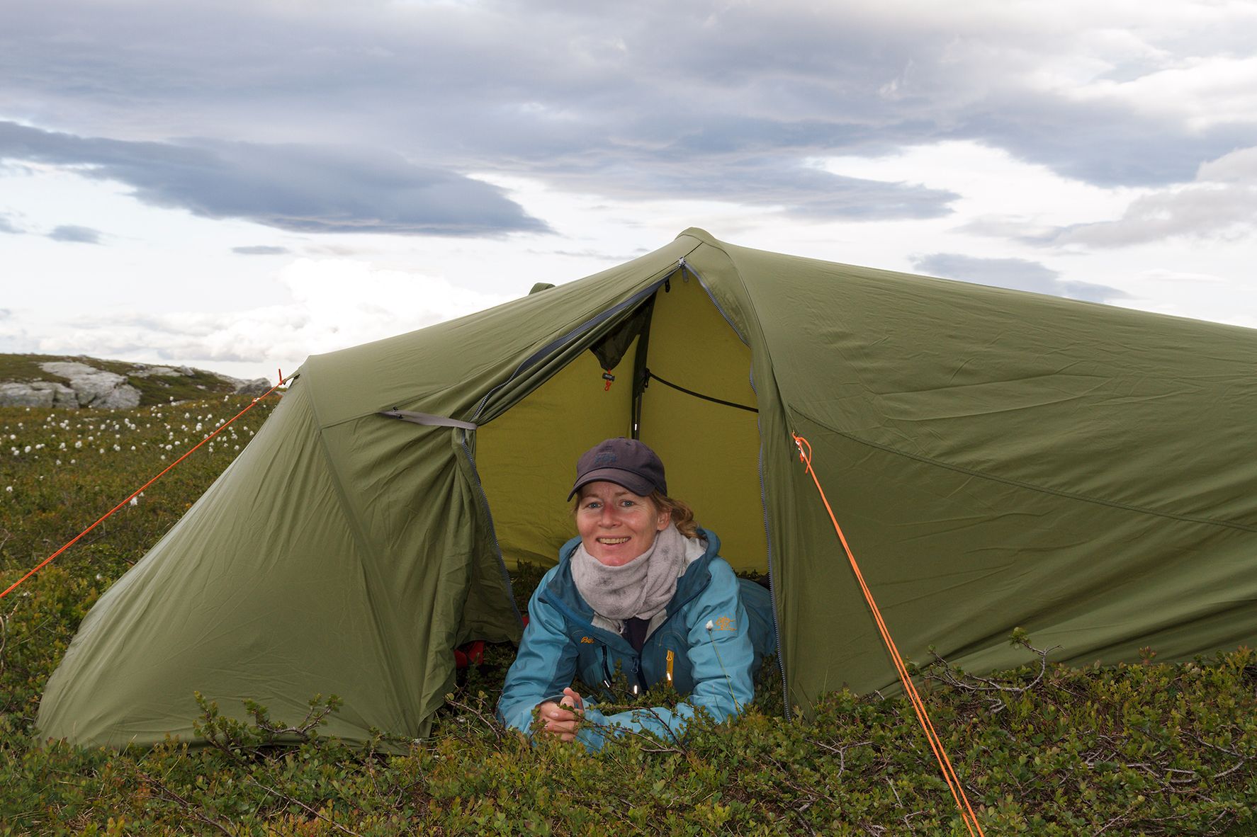 Kvinne ligger i teltåpningen, i fjellterreng